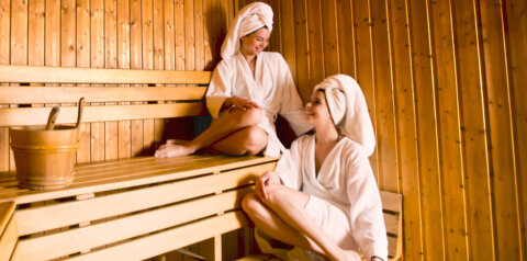 Zwei Personen sitzen im Bademantel und mit Handtuch auf dem Kopf in einer Sauna