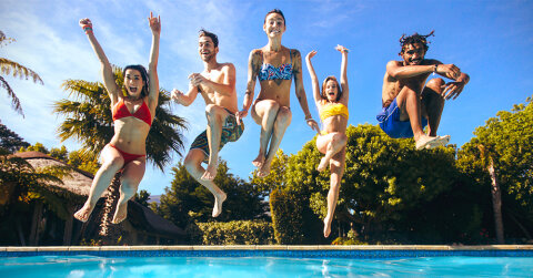 F&uuml;nf junge Menschen h&uuml;pfen freudig bei sch&ouml;nem Wetter in einen Pool